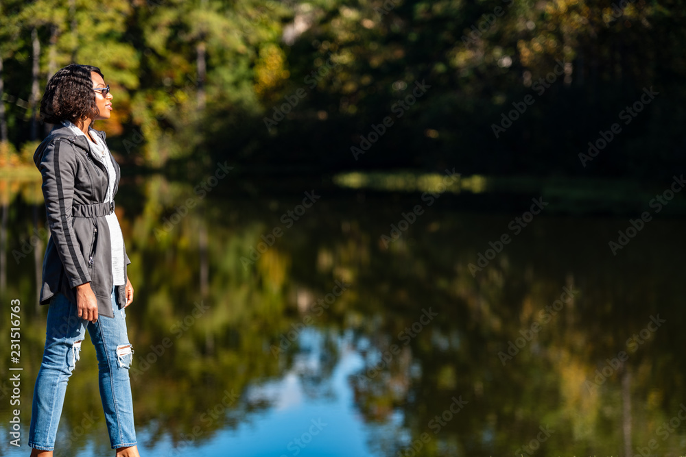 Beautiful young African-American Woman standing in front of lake in autumn Beautiful young African-American Woman standing in front of lake in autumn