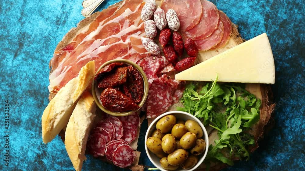 Delicious mix of different snacks and appetizers. Spanish tapas or italian antipasti on a wooden plate. View from above. Placed on blue table.