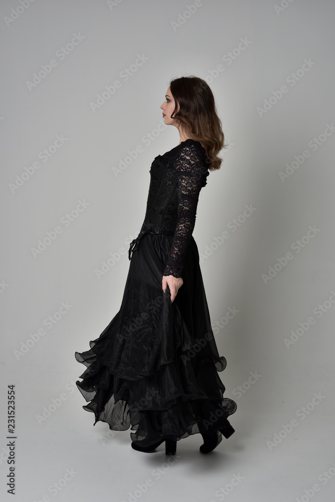 Fototapeta premium full length portrait of brunette girl wearing long black gown with corset. standing pose on grey studio background.