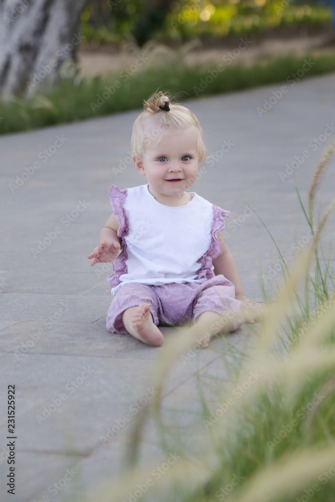 Adorable smiling baby girl sitting in the park pedestrian area Adorable smiling baby girl sitting in the park pedestrian area