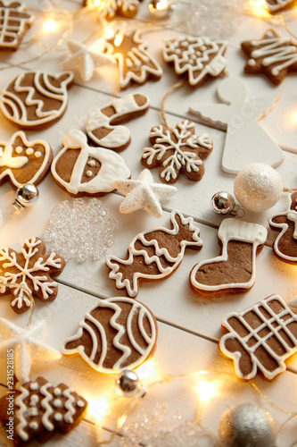 Christmas sweets composition. Gingerbread various shaped cookies with xmas decorations arranged on white wooden table with lights.