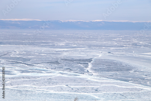 Cracks on the surface of the blue ice. Frozen lake in winter mountains. It is snowing. Lake Baikal. Winter