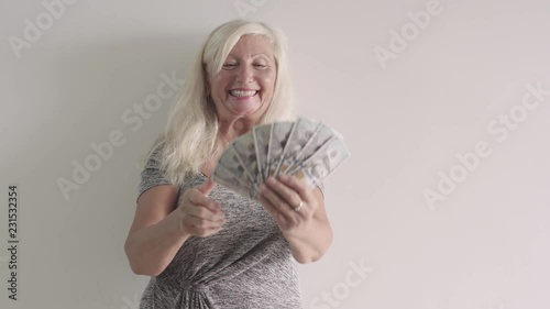 Old woman happy to get money, Blond Grandmother smiling and show her income. Retired lady holding a bundle of money (Dollars) in her hands. Shot with white backround. Finance and money concept