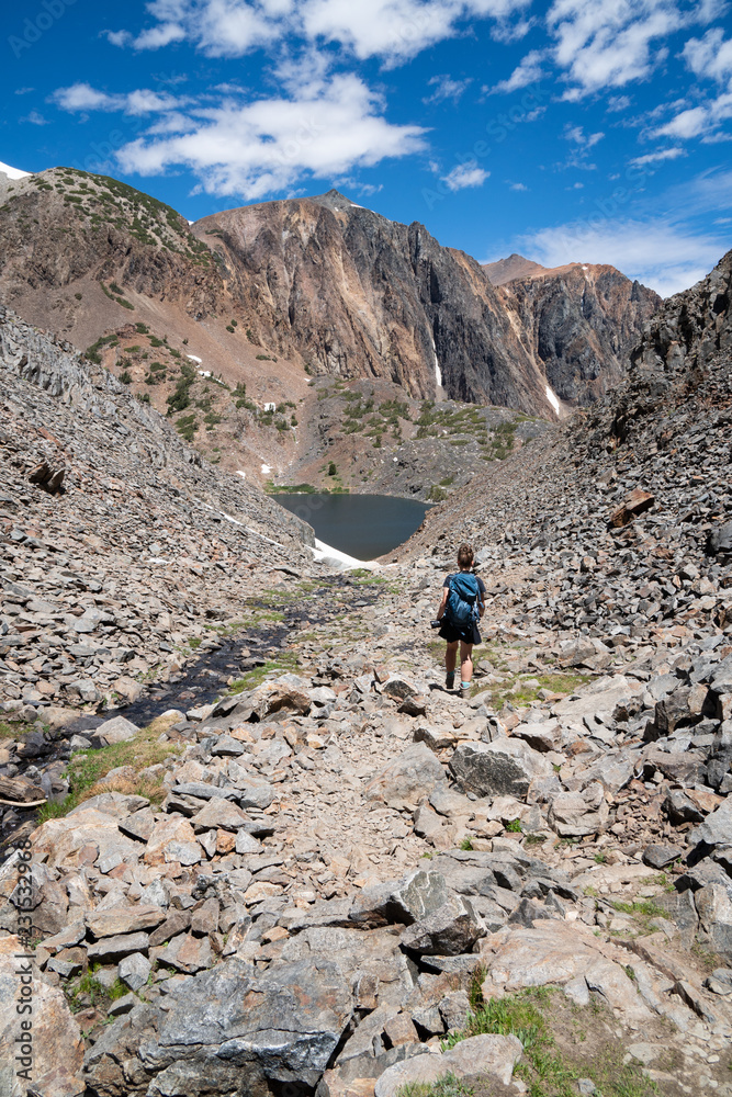 A female hiker makes her way down a dangerous hiking path of mountain scree and talus rocks in California Eastern Sierra Nevada mountains