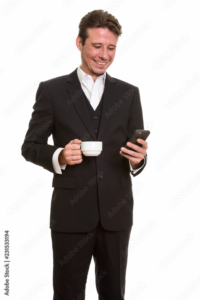 Happy Caucasian businessman using mobile phone while holding cof Happy Caucasian businessman using mobile phone while holding cof