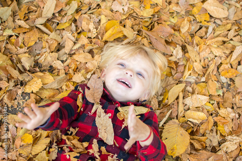 little girl with blue eyes is lying on the fallen leaves and playing merrily on an autumn sunny day