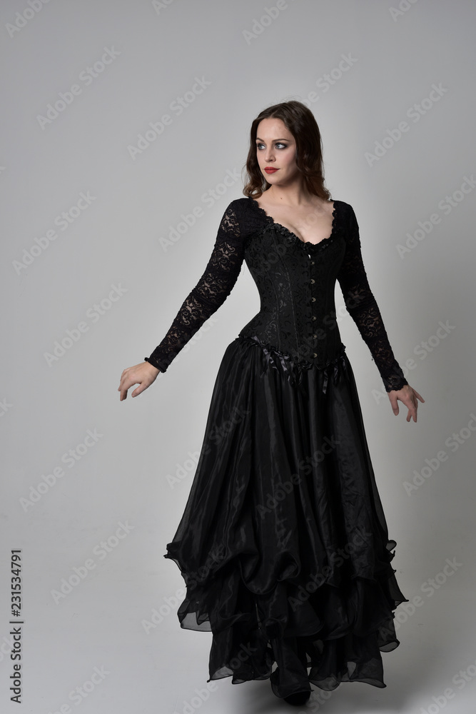 full length portrait of brunette girl wearing long black gown with corset. standing pose on grey studio background. full length portrait of brunette girl wearing long black gown with corset. standing pose on grey studio background.