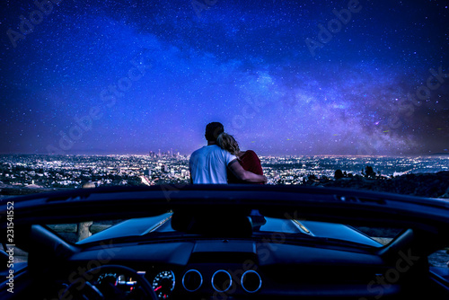 Couple watching sunset from popular view point in Los Angeles, California. Sitting on the sport convertible car hood photo