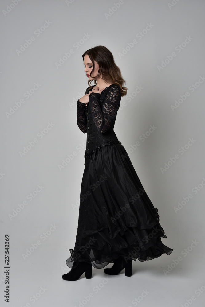 full length portrait of brunette girl wearing long black gown with corset. standing pose on grey studio background. full length portrait of brunette girl wearing long black gown with corset. standing pose on grey studio background.