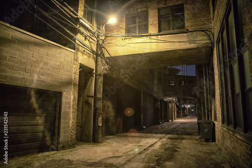 Dark and scary downtown urban city street alley scene with an eerie vintage industrial warehouse factory skyway at night photo