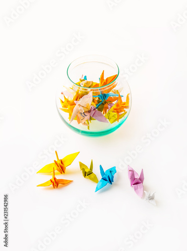 Small origami birds paper on white background and a glass jar filled with origami birds paper, top view