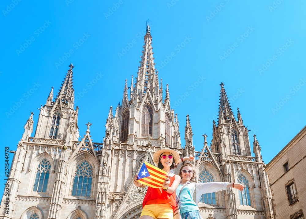 Fototapeta premium Dwóch turystów szczęśliwy kobieta zabawy i podróży z flagą katalońską w pobliżu katedry w Barcelonie