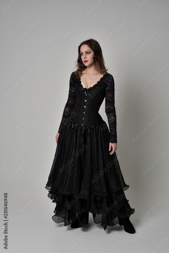 full length portrait of brunette girl wearing long black gown with corset. standing pose on grey studio background. full length portrait of brunette girl wearing long black gown with corset. standing pose on grey studio background.