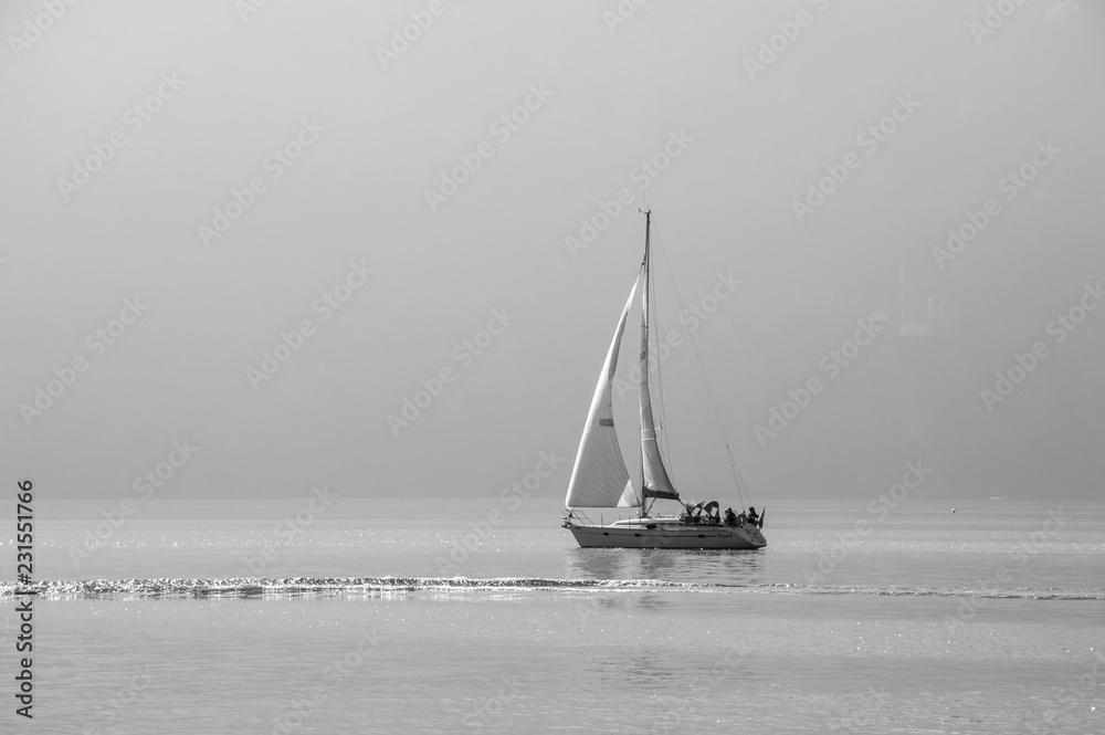 A romantic black and white picture of a sailing boat with a wave and the shimmering of the sun on Lake Lucern in Switzerland