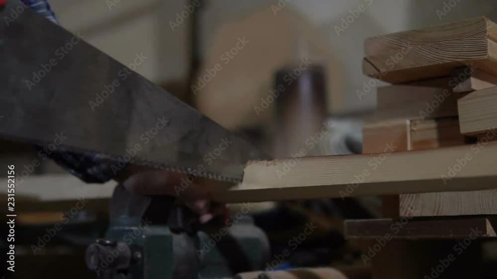 adult man saws a wooden Board, clamped in a Vice, in the workshop adult man saws a wooden Board, clamped in a Vice, in the workshop