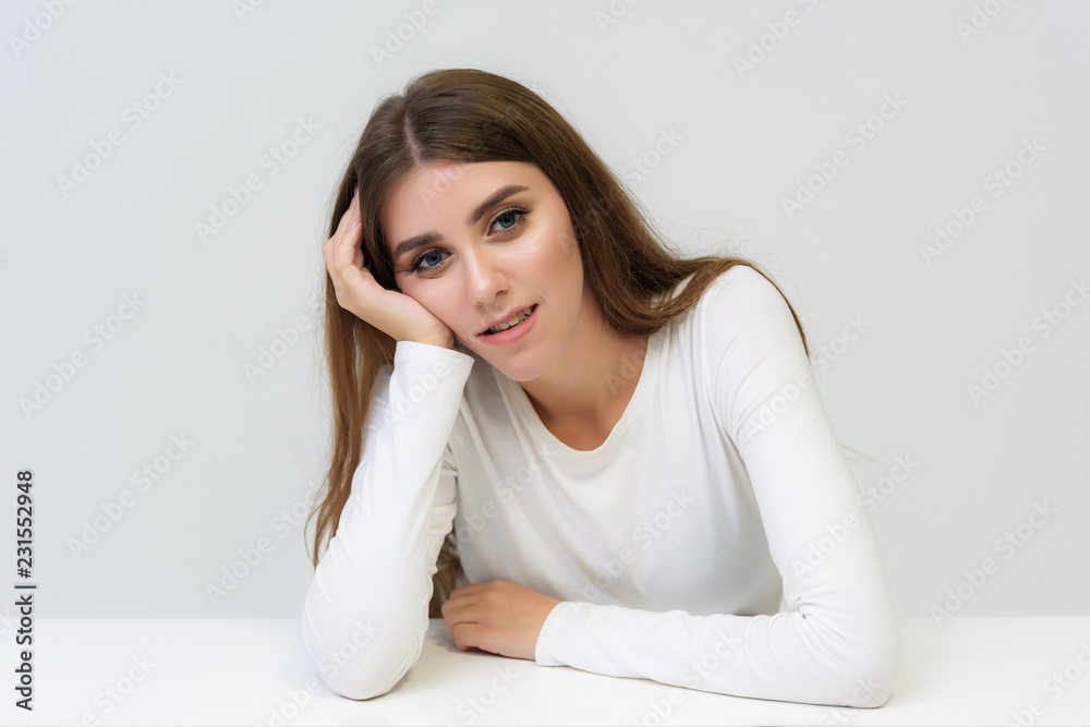 Studio portrait of a smiling happy beautiful brunette girl on a white background talking and sitting at the table. Studio portrait of a smiling happy beautiful brunette girl on a white background talking and sitting at the table.