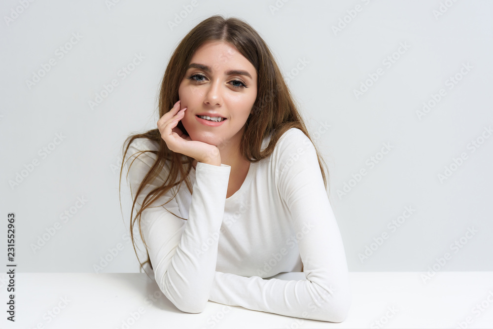 Studio portrait of a smiling happy beautiful brunette girl on a white background talking and sitting at the table. Studio portrait of a smiling happy beautiful brunette girl on a white background talking and sitting at the table.