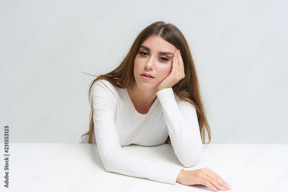Studio portrait of a smiling happy beautiful brunette girl on a white background talking and sitting at the table. Studio portrait of a smiling happy beautiful brunette girl on a white background talking and sitting at the table.