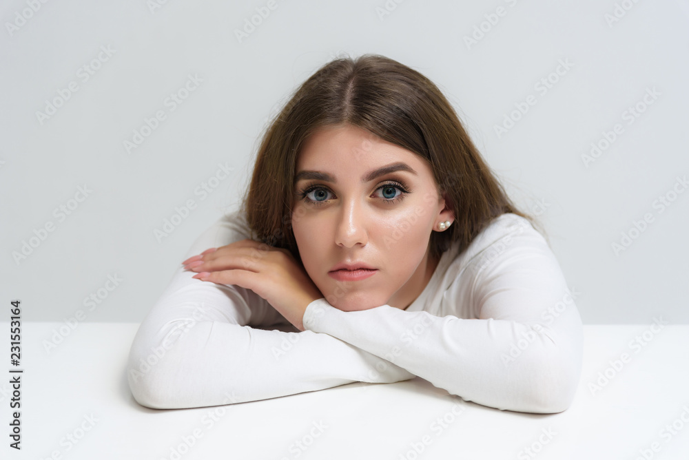 Studio portrait of a smiling happy beautiful brunette girl on a white background talking and sitting at the table. Studio portrait of a smiling happy beautiful brunette girl on a white background talking and sitting at the table.
