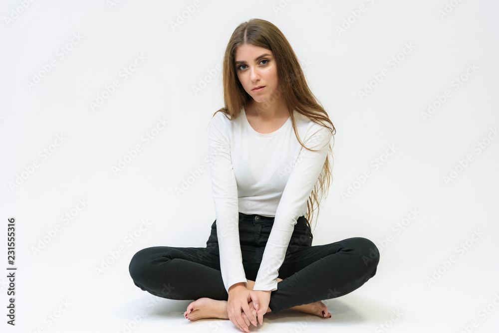 Studio portrait of a smiling happy beautiful brunette girl on a white background talking and sitting on the floor. Studio portrait of a smiling happy beautiful brunette girl on a white background talking and sitting on the floor.