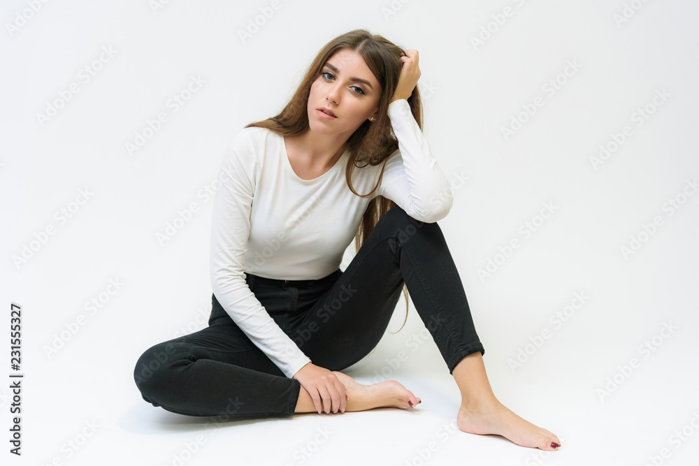 Studio portrait of a smiling happy beautiful brunette girl on a white background talking and sitting on the floor. Studio portrait of a smiling happy beautiful brunette girl on a white background talking and sitting on the floor.