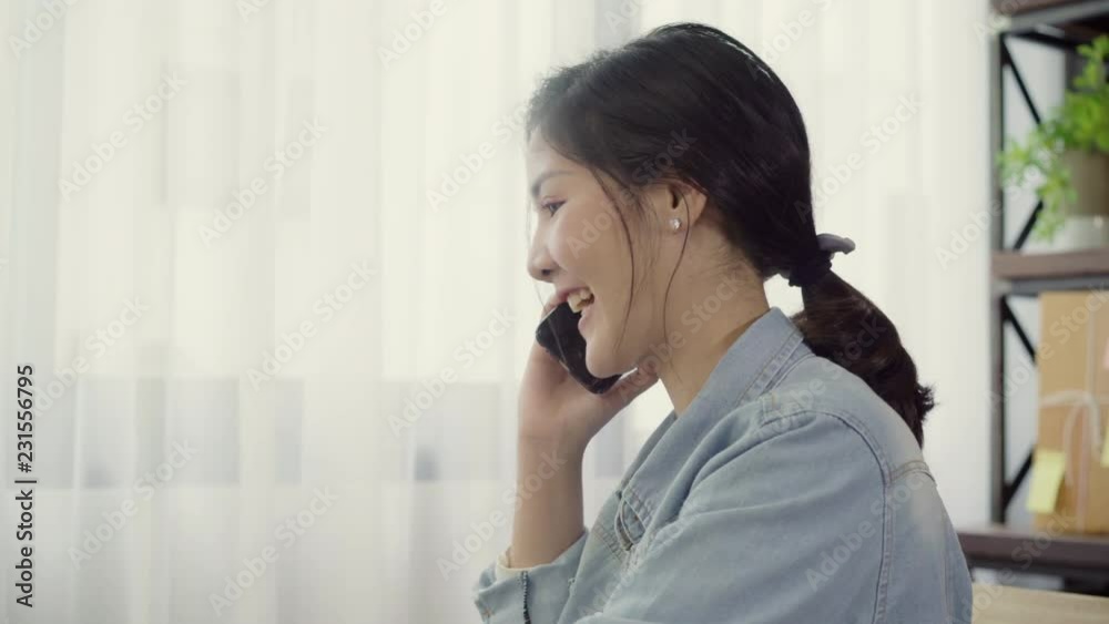 Beautiful smart Asian young entrepreneur business woman owner of SME online using smartphone call receive from customer and using laptop working at home. Small business owner at home office concept. Beautiful smart Asian young entrepreneur business woman owner of SME online using smartphone call receive from customer and using laptop working at home. Small business owner at home office concept.