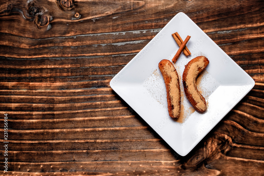 fried banana served on white square plate with cinnamon and sugar, over dark wood fried banana served on white square plate with cinnamon and sugar, over dark wood