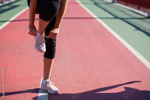 Young athletic model tying shoelace at the running track in sunny day. Empty space