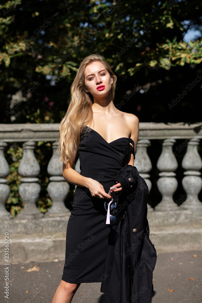 Fashionable blonde lady with long hair and red lips wearing black dress,  takes off her coat Stock Photo | Adobe Stock