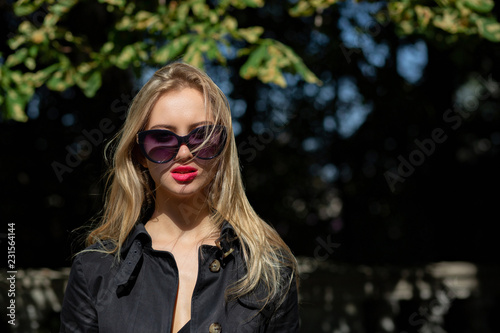 Lifestyle shot of adorable blonde model with reb lips wearing sunglasses. Space for text