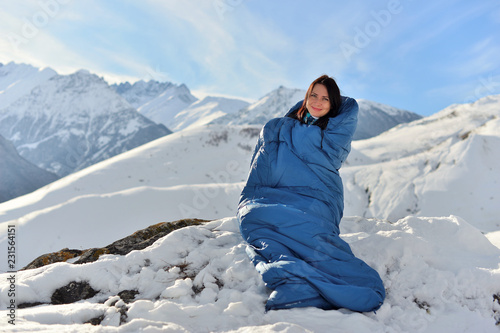 Happy woman in sleeping bag in snowy mountains in winter.