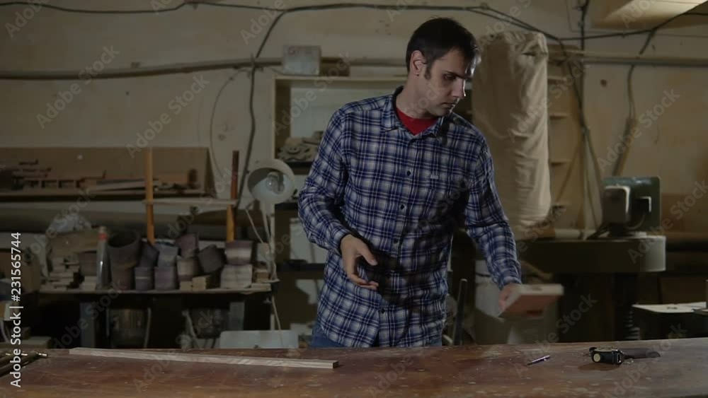 Worker in work shirt measures wooden board with long yellow ruler on a workbench Worker in work shirt measures wooden board with long yellow ruler on a workbench