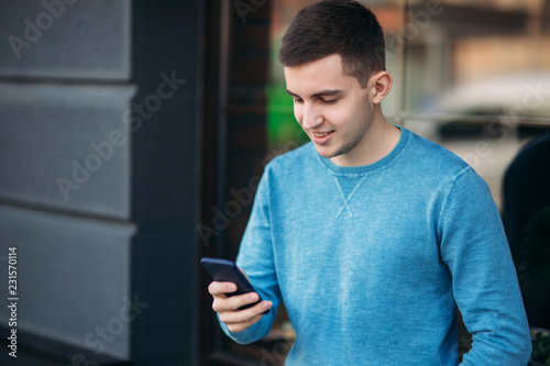 Young man is using the phone on the street. Handsome guy stand in front of window