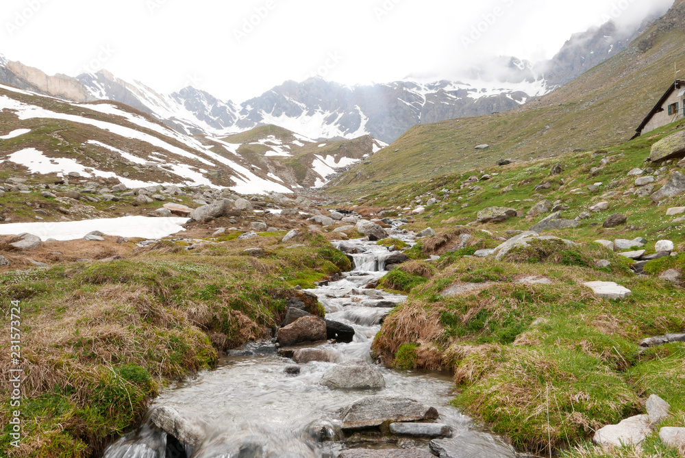 Mountain river descending from glacier, surrounded by wild environment on foggy day. - Grand Paradis National Park, Cogne Valnontey, Aosta Valley, Italy