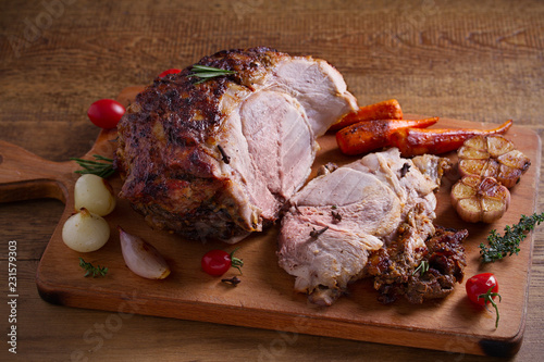 Baked ham with vegetables, rosemary and thyme on chopping board. horizontal