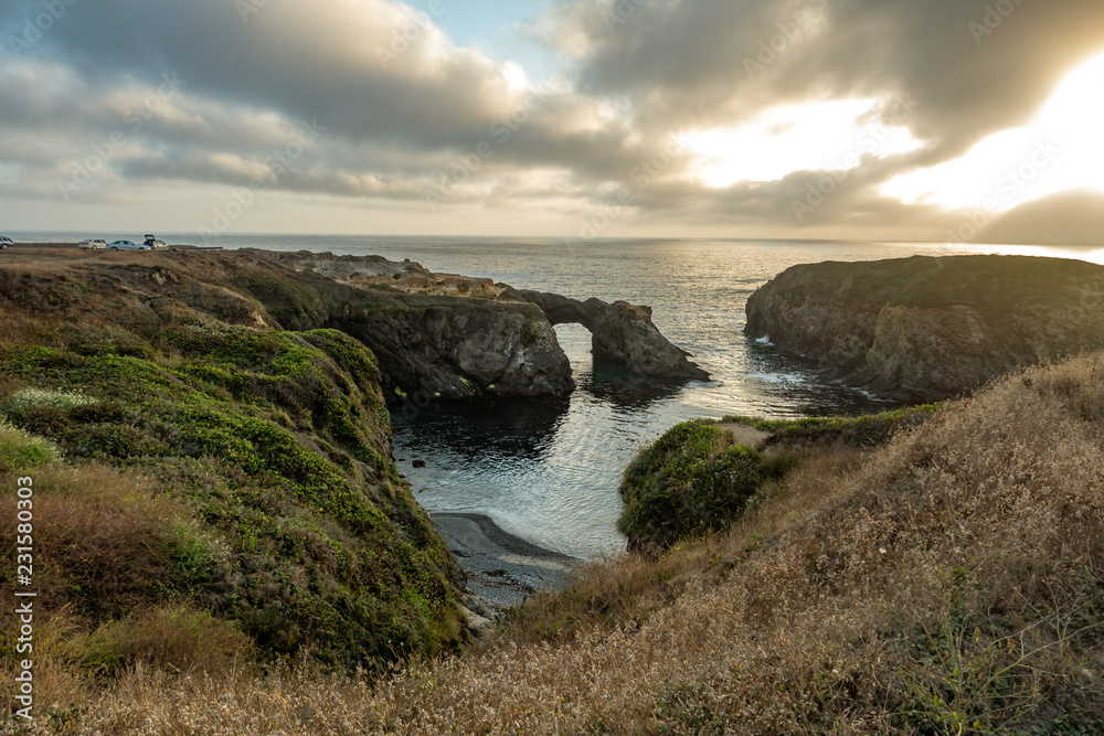 Rock arch and the rugged Pacific at sunset with dramatic clouds