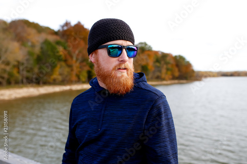 Redheaded man standing on bridge over lake