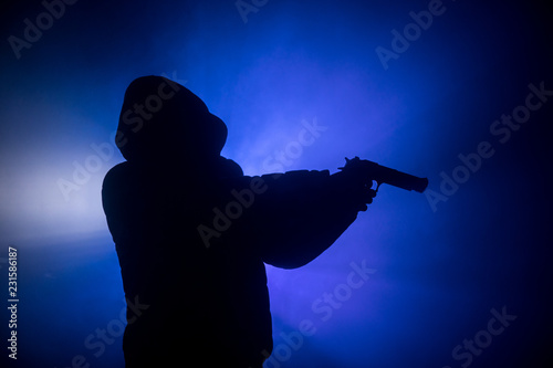 Silhouette of man with assault rifle ready to attack on dark toned foggy background or dangerous bandit in black wearing balaclava and holding gun in hand. Shooting terrorist with weapon theme decor