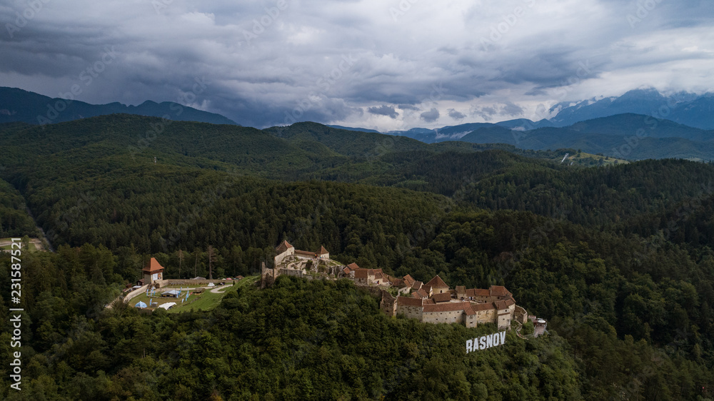 Aerial landscape of Rasnov Castle, with Bucegi massif in Carpathian Mountains on a sunny day.