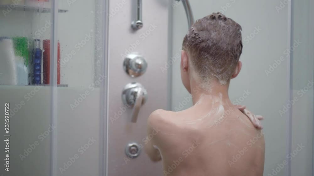 Young boy bathing under a shower at home - back view. Beautiful teen boy taking shower and washing in the bathroom. Happy child washing head, face and body with water. Stock-Video | Adobe Stock