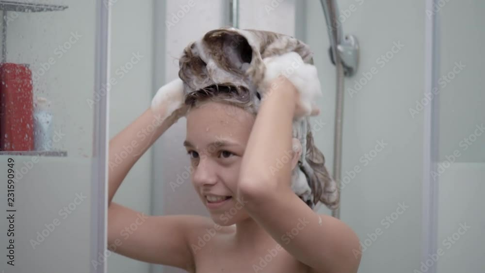 Vídeo do Stock: Smiling young girl bathing under a shower at home. Beautiful teen girl taking shower and washing in the bathroom. Happy child washing head, face and body with water. | Adobe Stock 