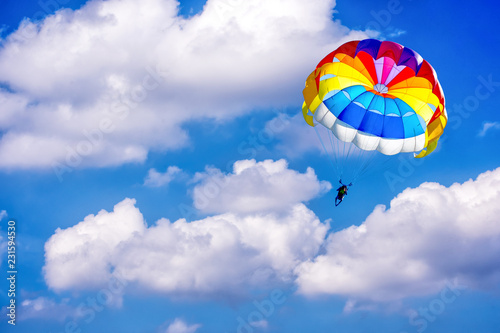 A man is gliding using a parachute on the background of cloudy blue sky.