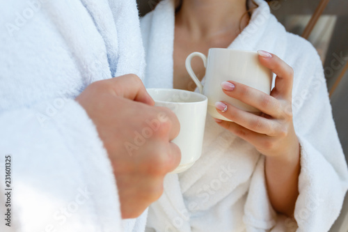 Happy young couple in white bathrobes drinking coffee and fresh juice together in bed in the morning. The couple meet in the morning at the hotel. Morning breakfast in the room.