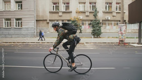 Young hipster man in helmet riding fixed gear bicycle in the city during autumn morning, side view photo