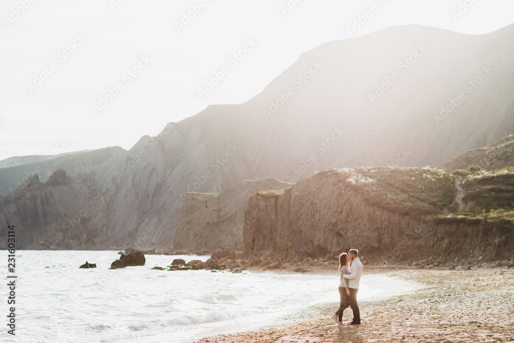 Couple walking by empty sand beach with amazing mountain view with rocks and green hills. Nordic nature