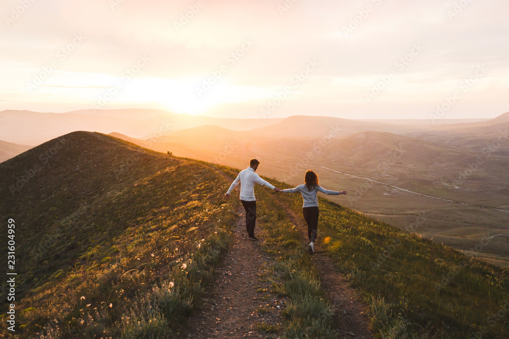Young couple running together by sunset hill with amazing mountain view