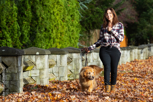 Woman walking golden retriever dog in Fall leaves