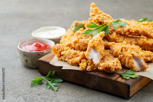 Foto Breaded chicken strips with two kinds of sauces on a wooden Board