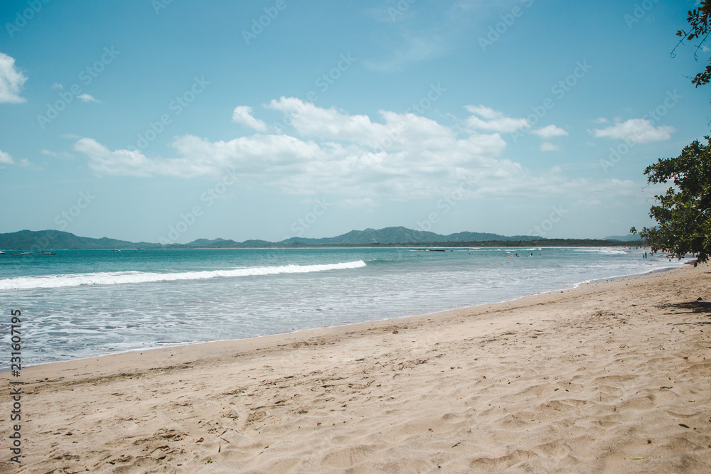 Empty sandy beach of Tamarindo with turquoise waves and mountains around the bay