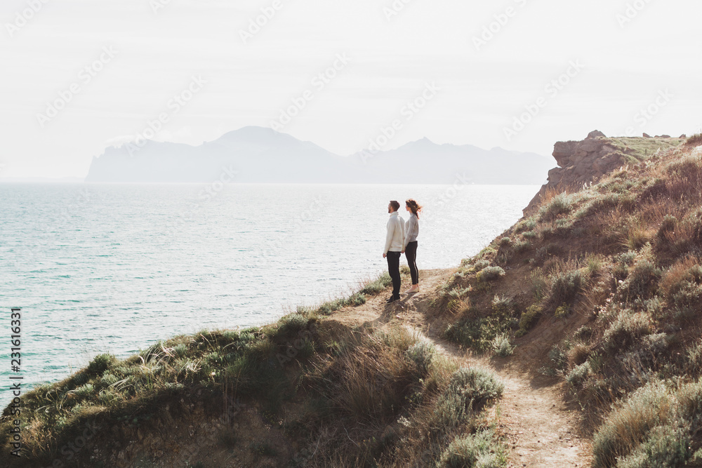 Young couple walking on nordic sea coast with mountain view in spring, casual style clothing sweaters and jeans